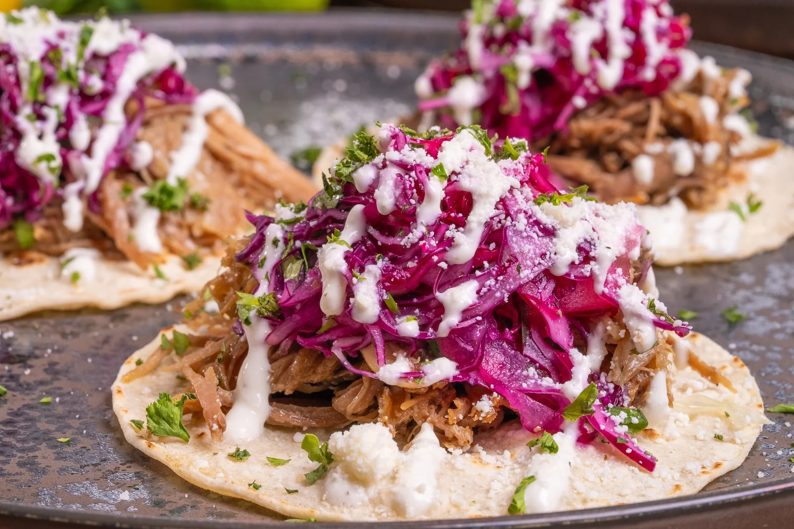 Carnitas tacos topped with pickled red cabbage and crema on a metal tray
