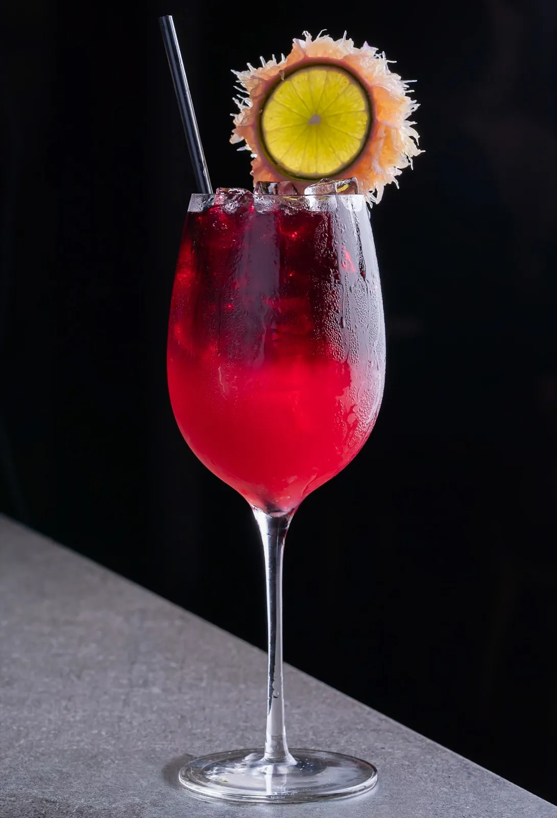 A red cocktail with a citrus garnish, shot on black for a drinks menu