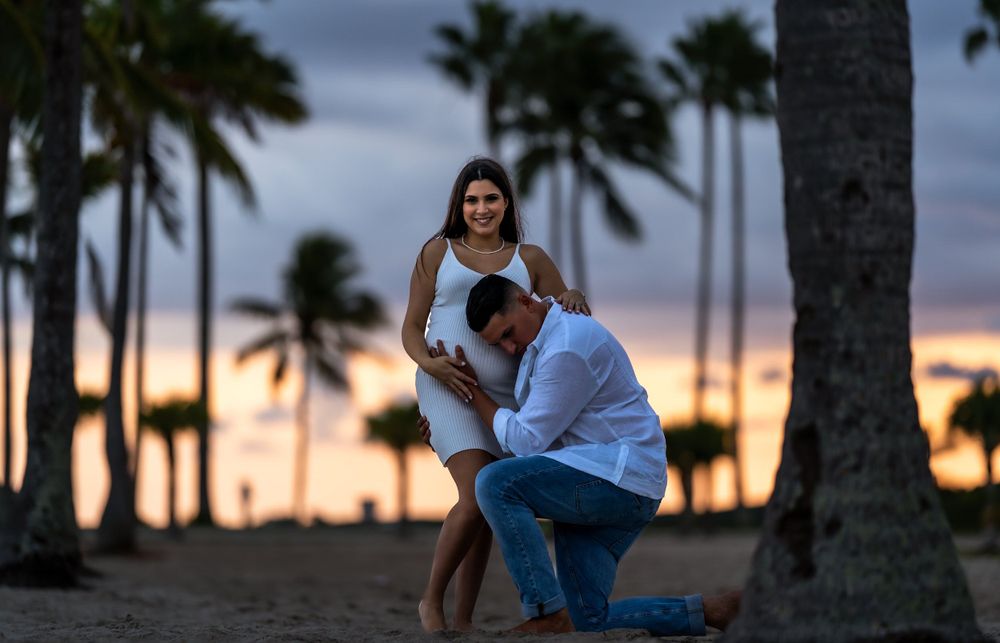 Expecting couple at sunset on the beach, he kneels in front of her among the palm trees