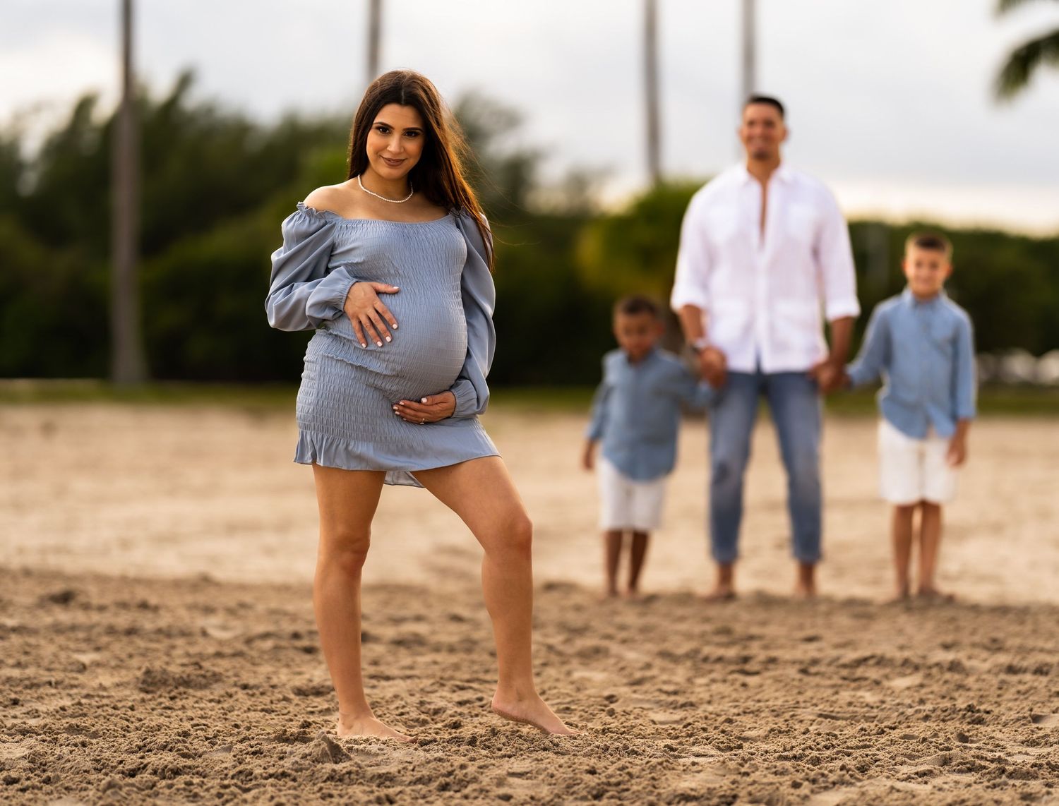 Expecting mother with her partner and their two young sons on the beach at sunset