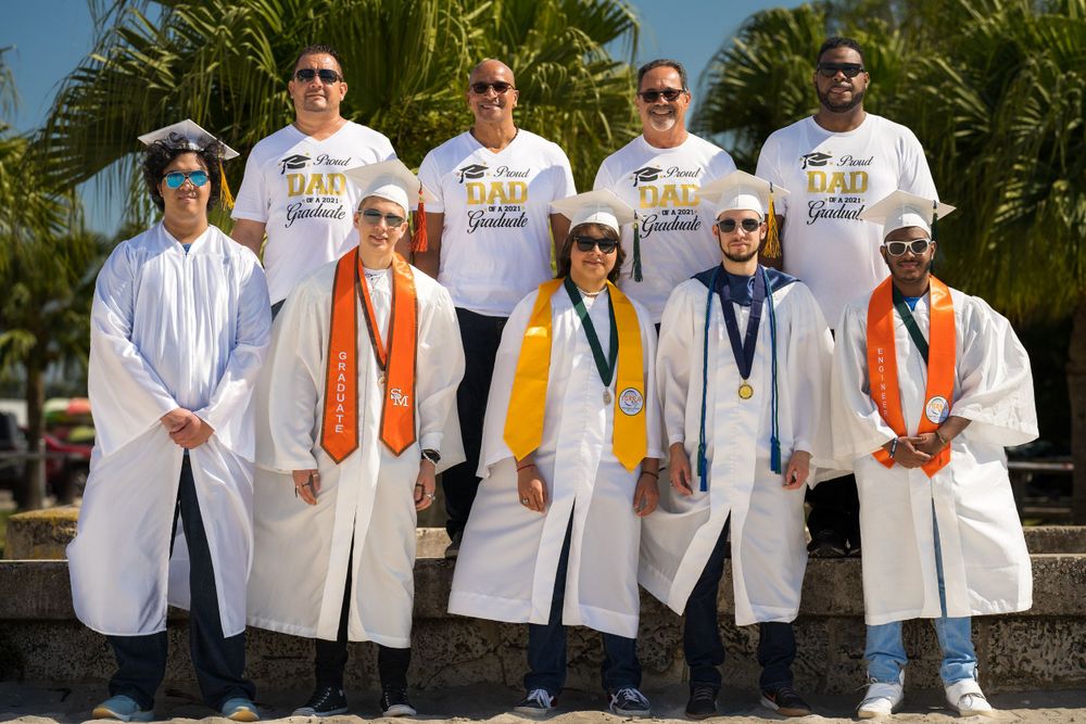 Large group of graduates in caps, gowns, and orange cords posing together outdoors