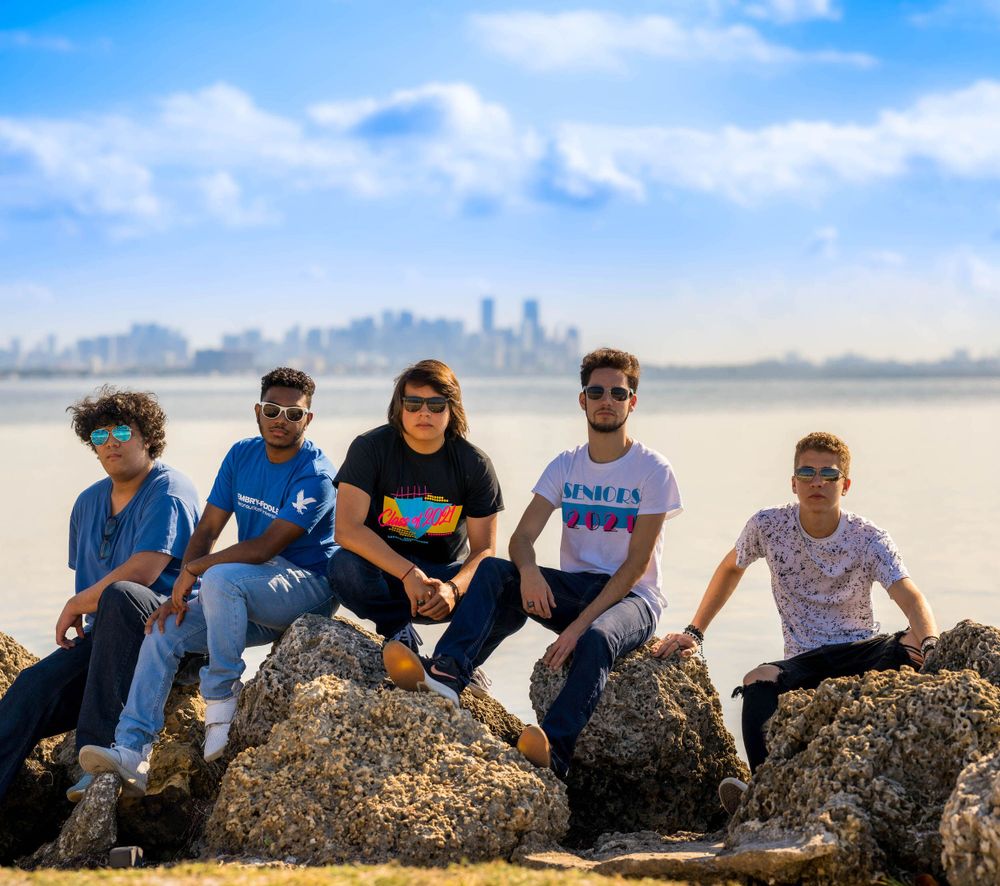 Group of six friends sitting together on the rocks along the Miami waterfront with the skyline behind them