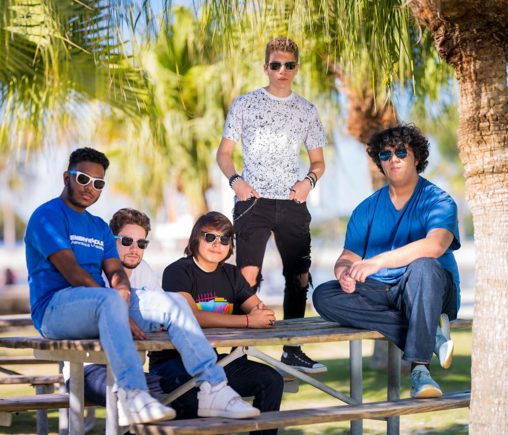 Group of four friends posing on a picnic table under palm trees