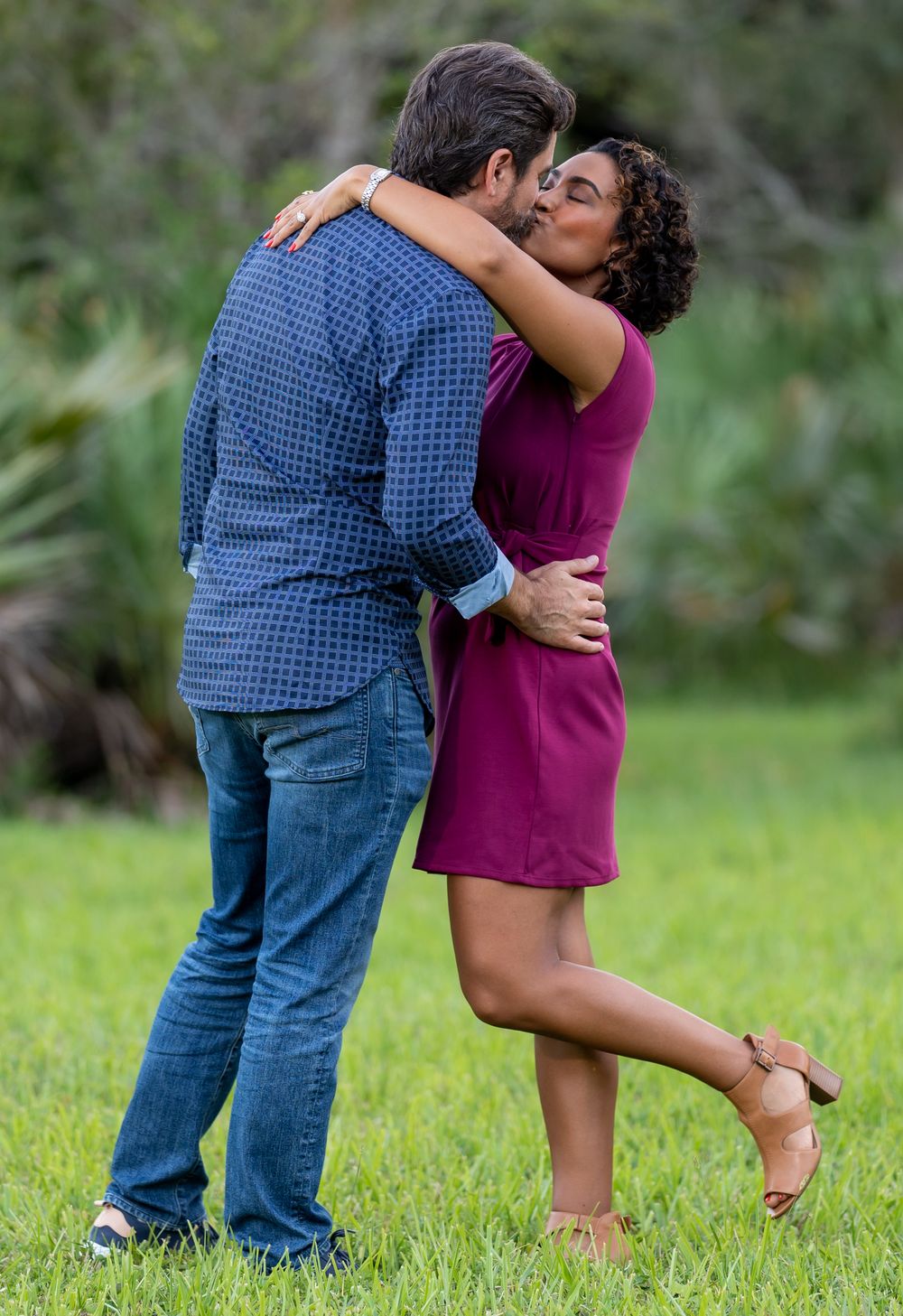 A couple kissing in a grassy park, her heel kicked up behind her