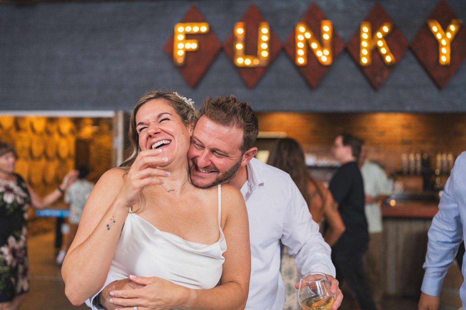 Bride laughing mid-toast while the groom nuzzles her at the reception bar