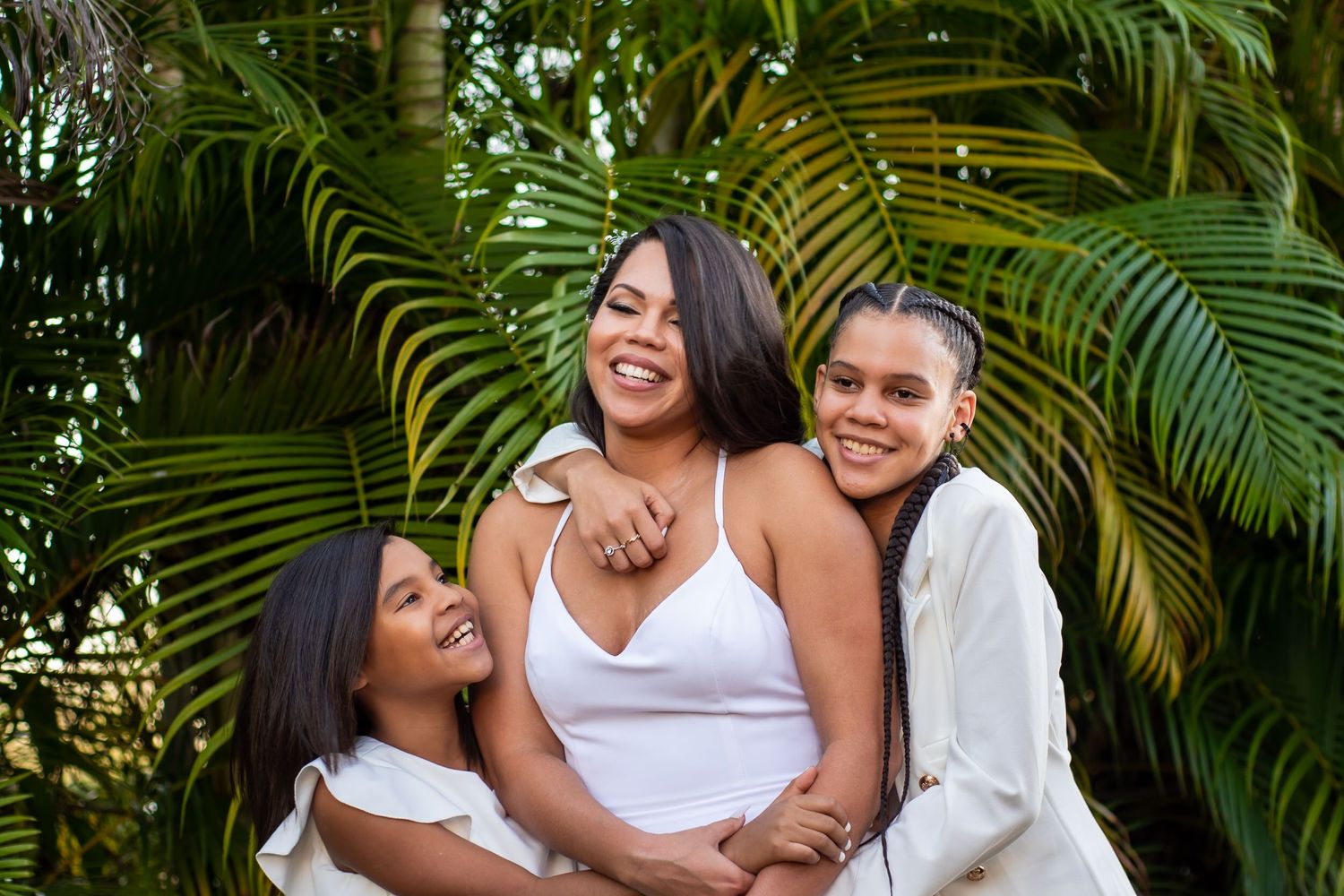 Bride laughing with two young bridesmaids in white, palm fronds framing the shot