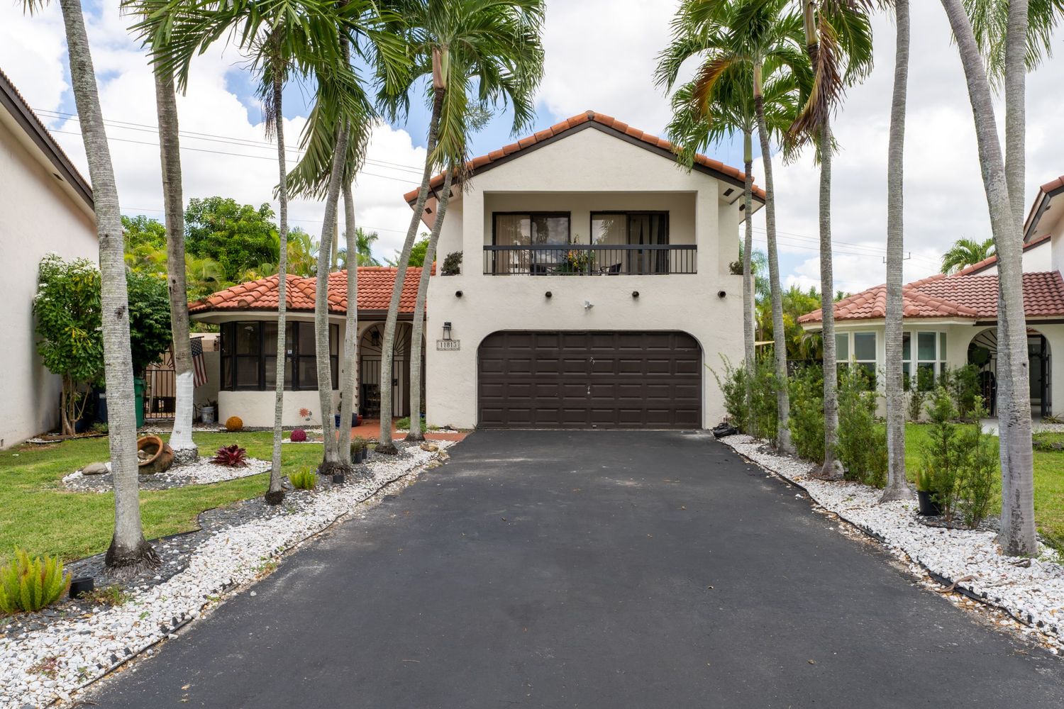 Two-story single-family home exterior with a paved driveway, palm trees, and a car parked in front