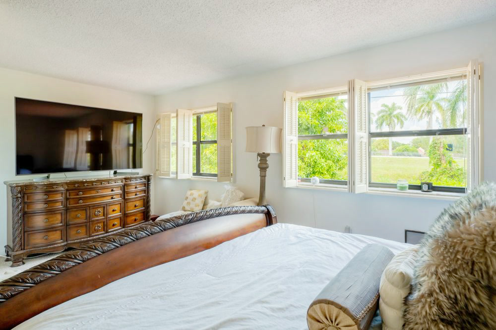 Bedroom with plantation shutters, a wall-mounted television, and natural light