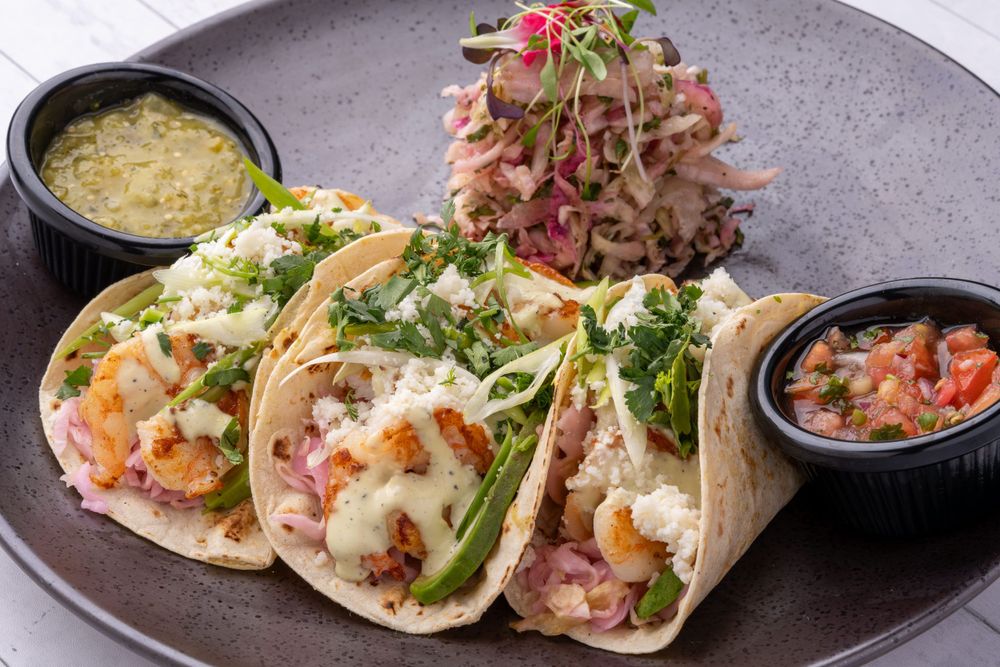 Three fish tacos with salsa and guacamole