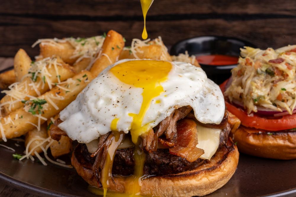 A burger topped with a fried egg, yolk running