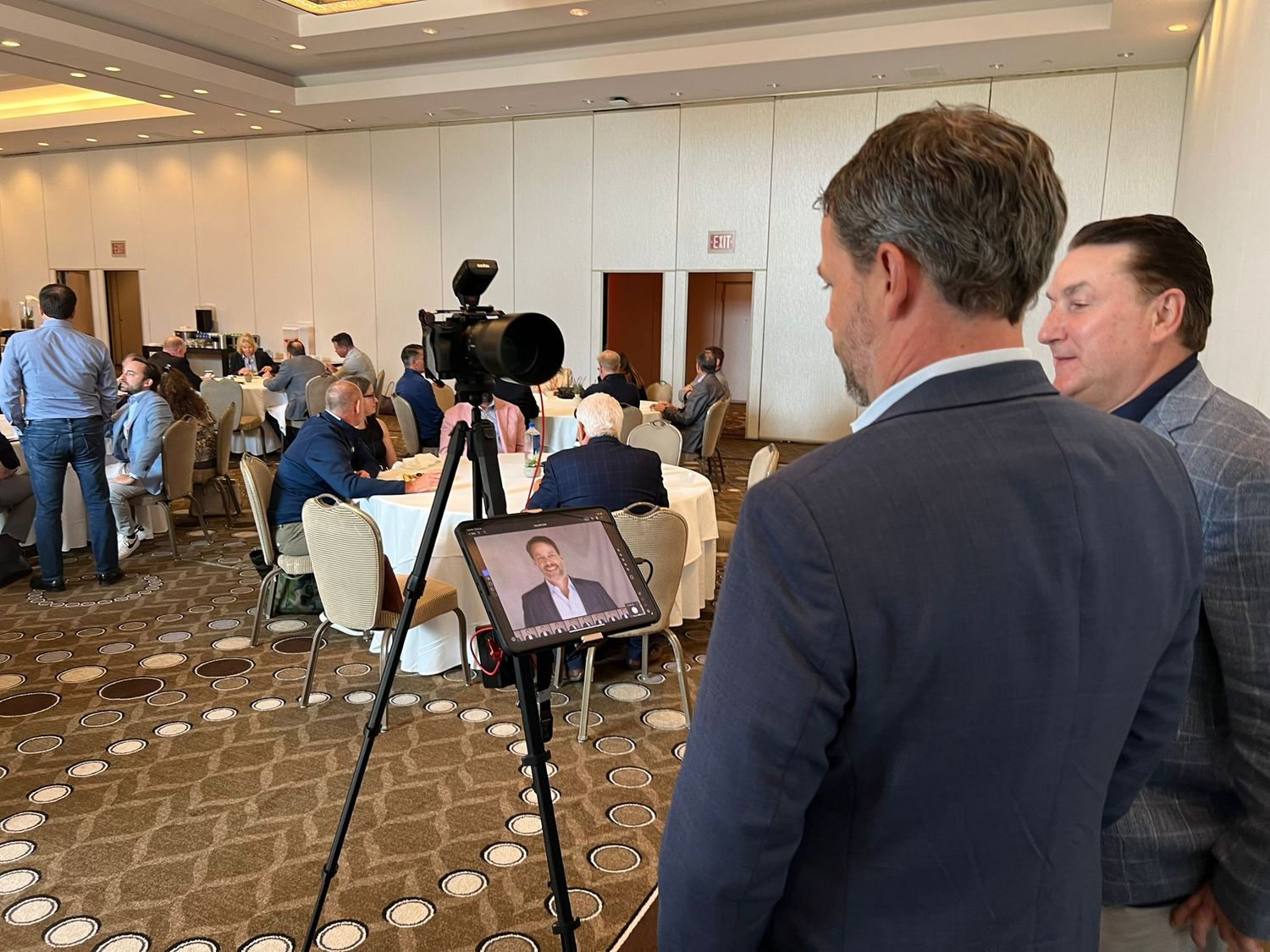Camera on a tripod filming a ballroom of round tables at a corporate event
