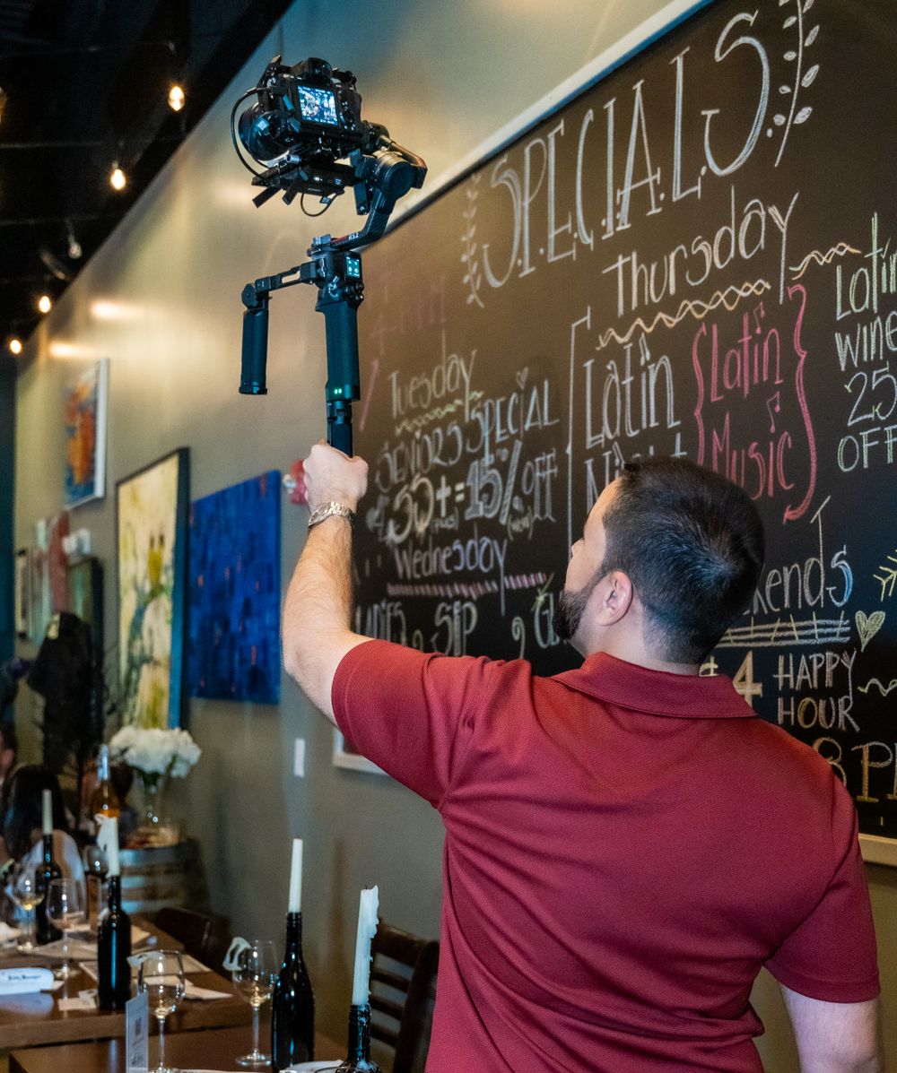 Our operator lifting a gimbal camera in front of a restaurant chalkboard menu