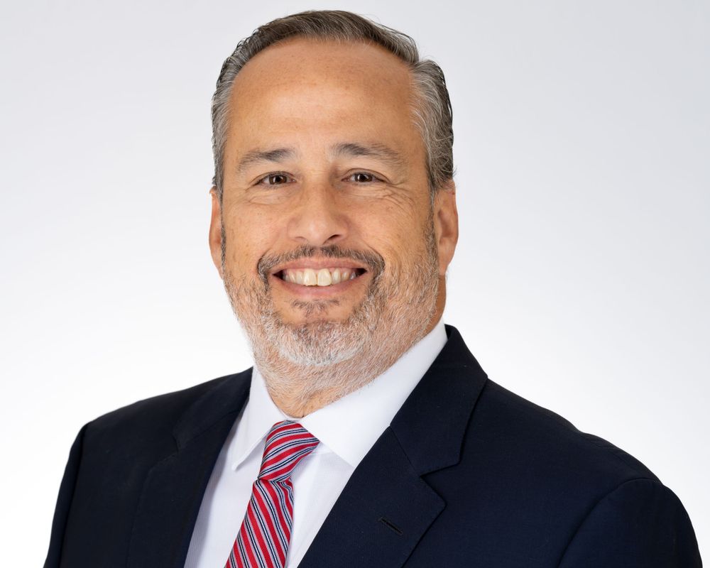 Studio headshot on white, smiling man in a navy suit and striped tie