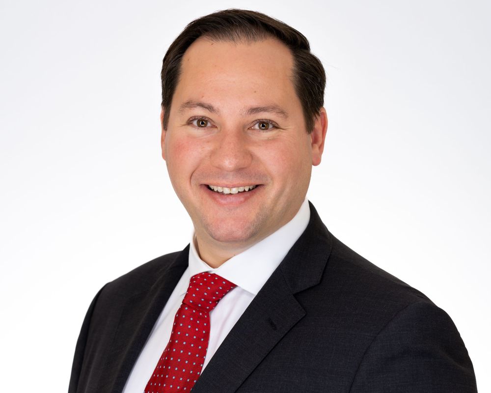 Studio headshot on white, smiling man in a black suit and red tie