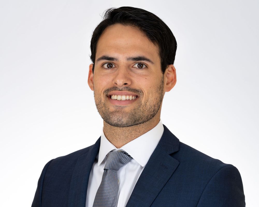 Studio headshot on white, man in a navy suit and gray tie