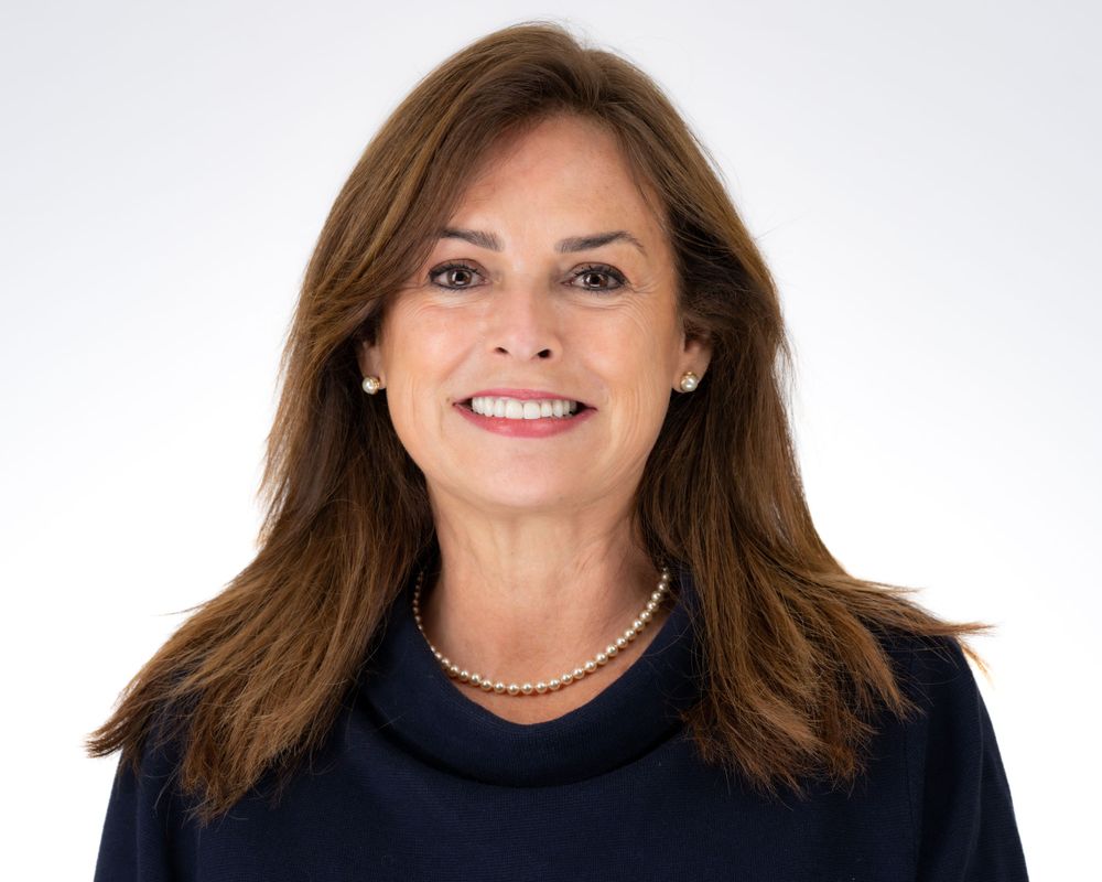 Studio headshot on a soft gray backdrop, navy sweater and pearl necklace
