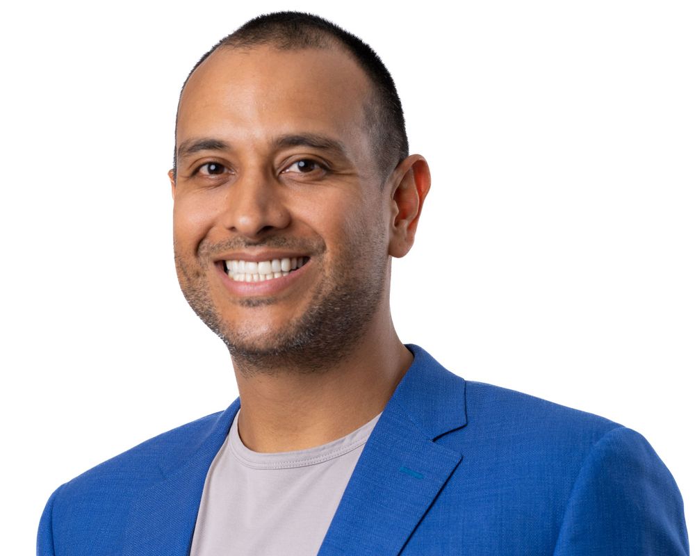 Studio headshot on white, smiling man in a bright blue blazer