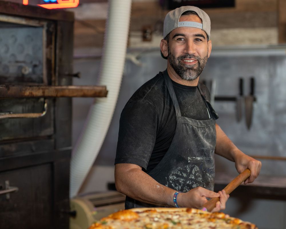 On-location headshot of a chef holding a fresh pizza in front of the oven