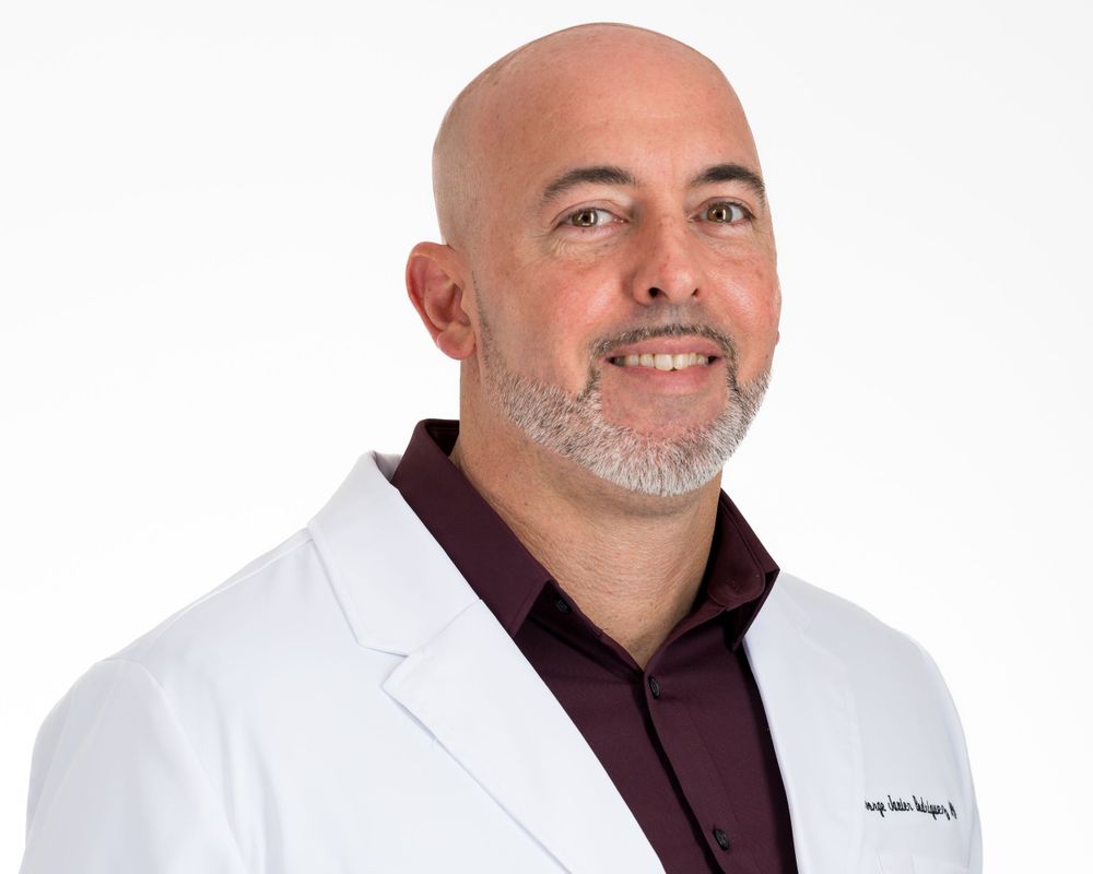 Studio headshot on white, bald man with a gray beard in a white coat