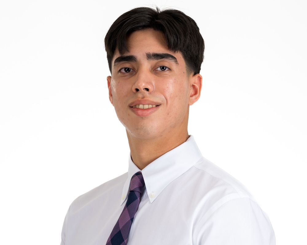 Studio headshot on white, young man in a white shirt and plaid tie