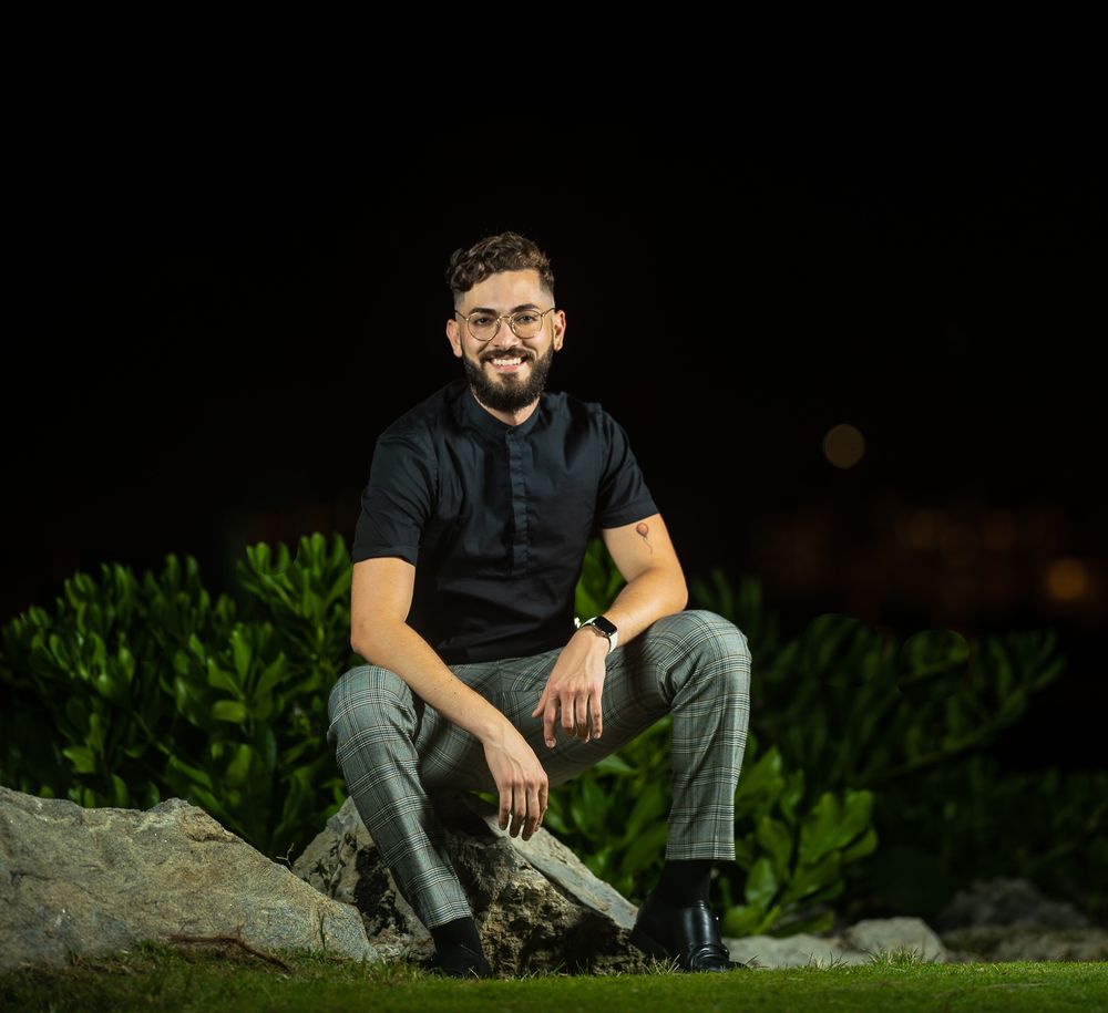 Male model seated on rocks at night with city lights softly blurred in the background