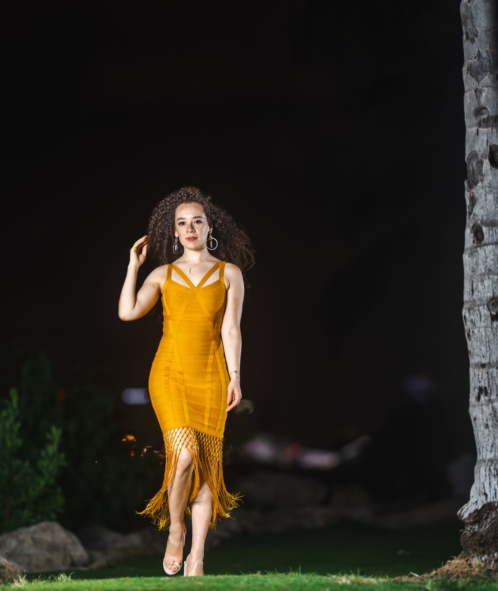 Model in a mustard yellow fringe dress walking through a grassy area at night
