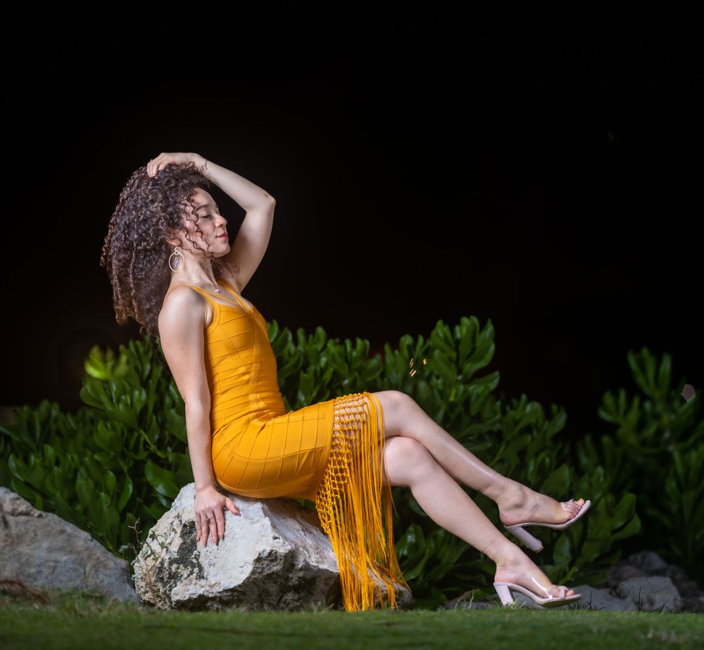 Model in a mustard fringe dress seated on a rock at night with her hair falling over her shoulder