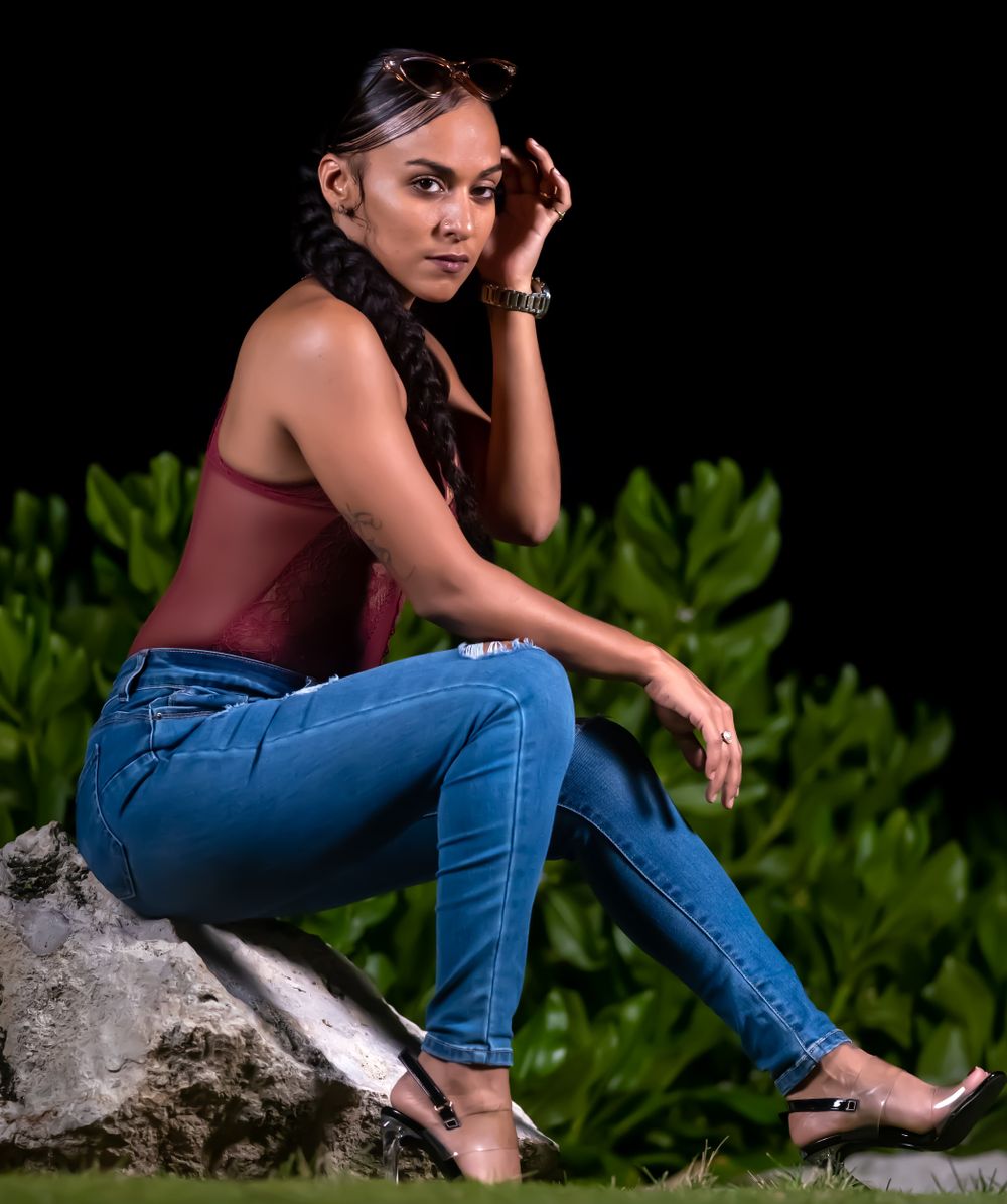 Model in a burgundy top and jeans sitting on a rock at night with a hand raised to her hair