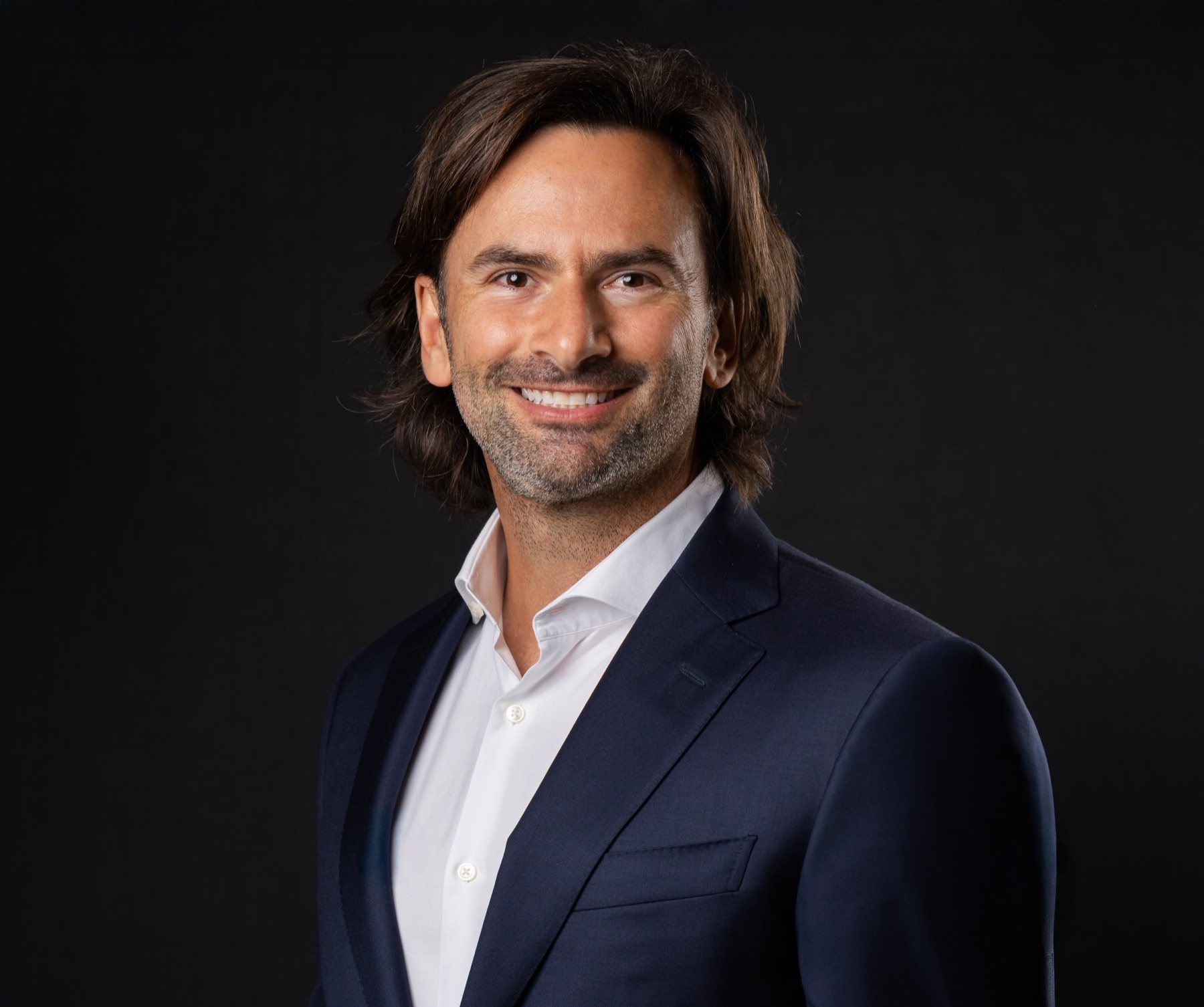 Professional headshot portrait in a navy suit against a dark studio backdrop