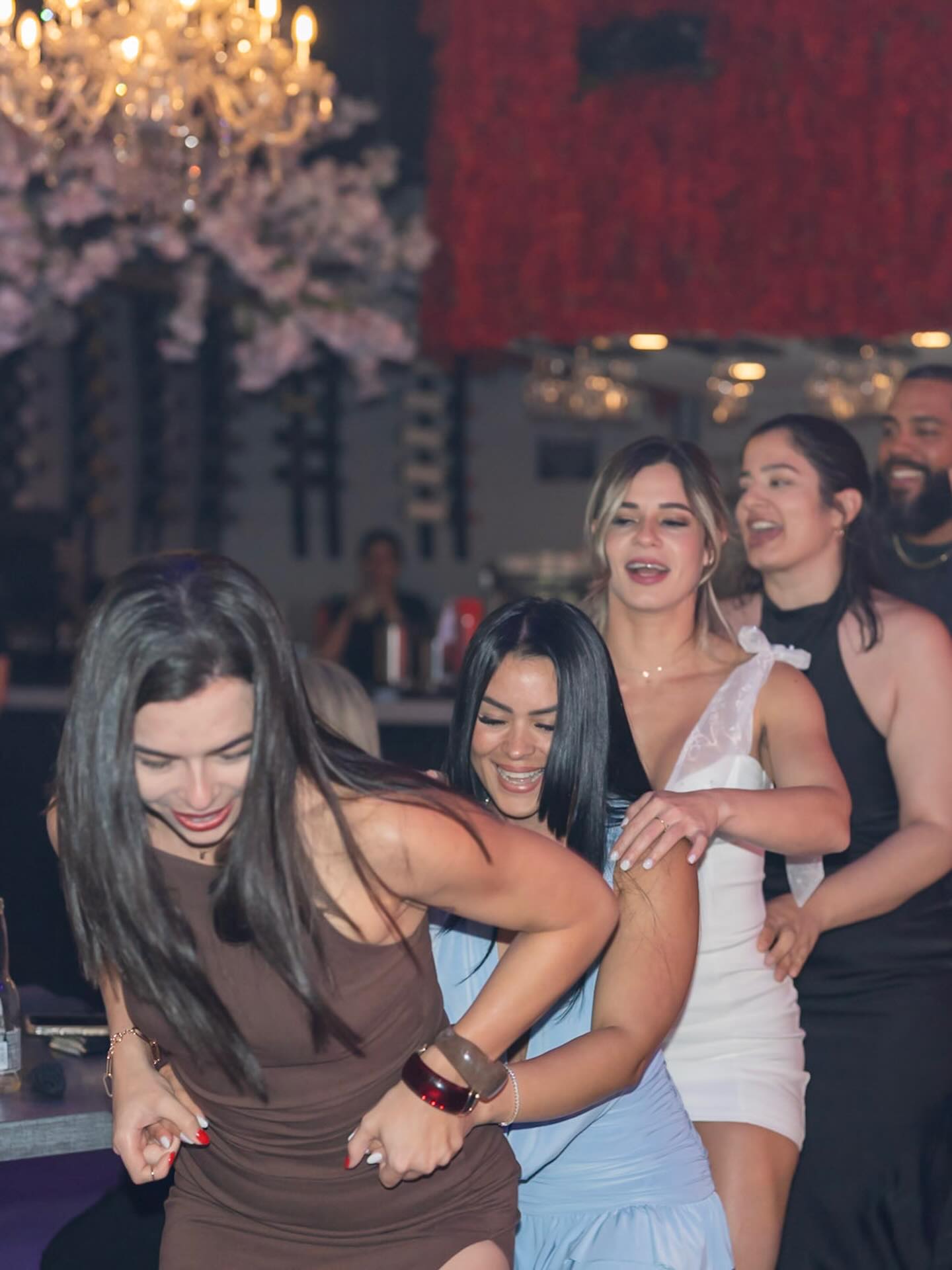 Friends dancing in a line at a lively bar under a chandelier